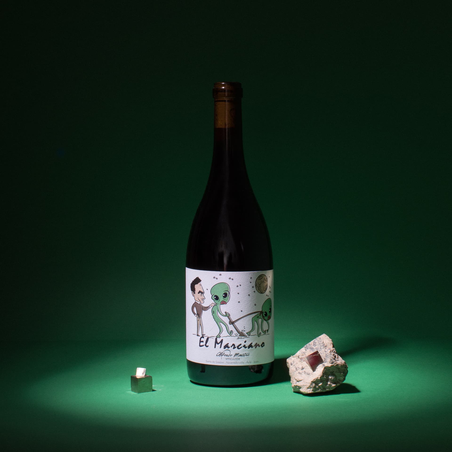 Botella de vino natural sobre superficie verde, junto a dos minerales